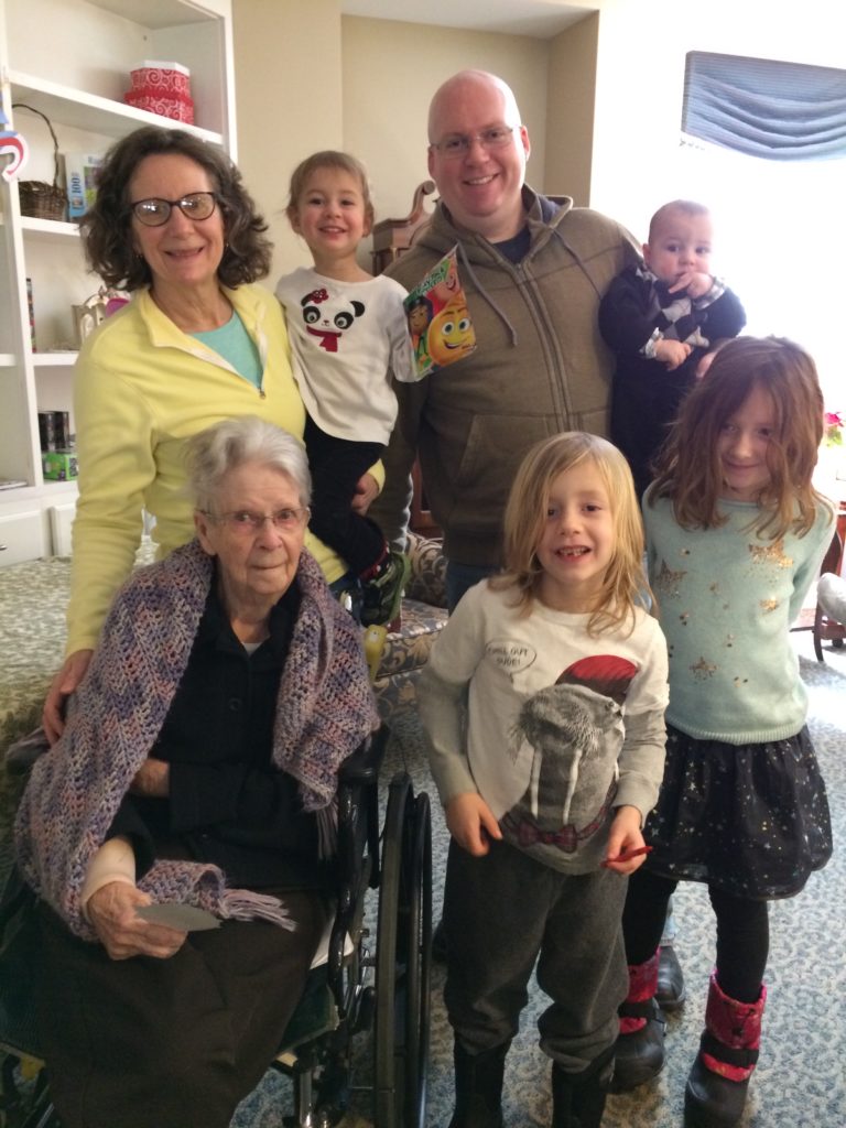 A photograph of Grandma, Mimi, Kevin, Rayleigh, Dillon, Ainsley, and Grayson at Grandma's nursing home.