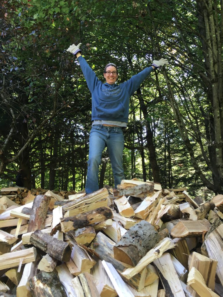 Kelsey standing on top of a pile of unstacked wood with her hands over her head.