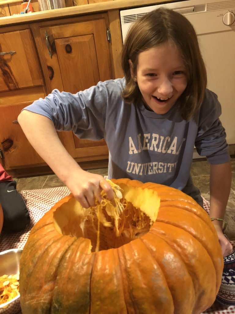 Rayleigh squishing a handful of pumpkin guts with a gleeful expression.