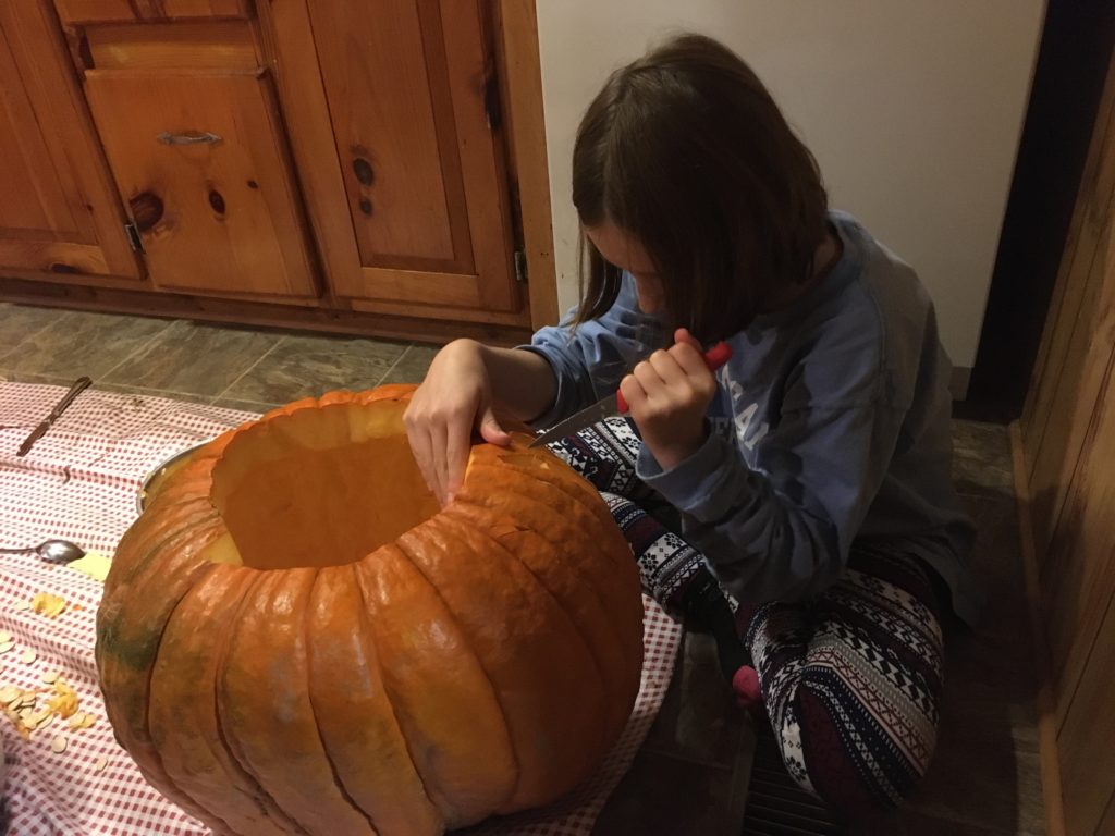 Rayleigh carving her pumpkin on the kitchen floor.