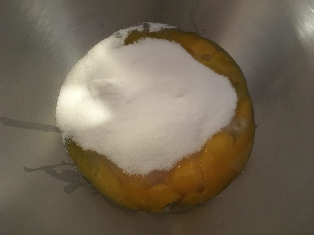 A photo of eight egg yolks and one cup of sugar in a mixing bowl.