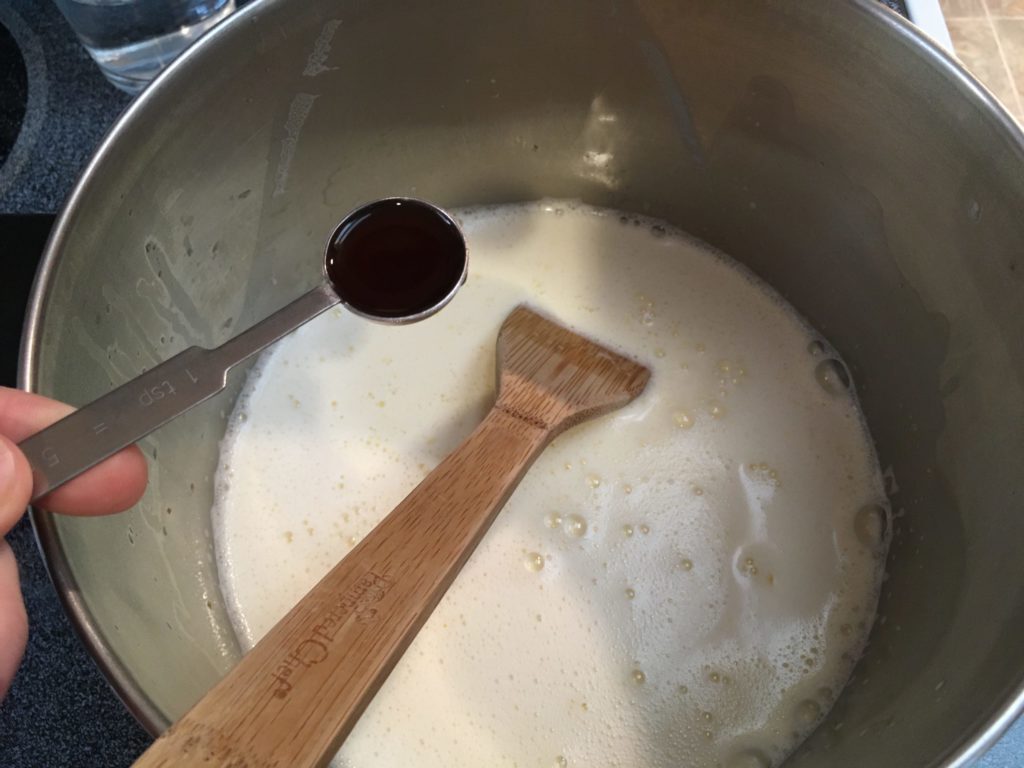 A photo of the liquid ice cream in the cookpot with a teaspoon of vanilla about to be added.