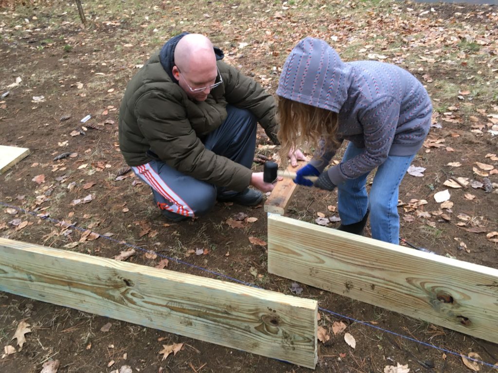 A photo of Dillon hammering in a support stake for the rink wall while Kevin holds the installation tool.