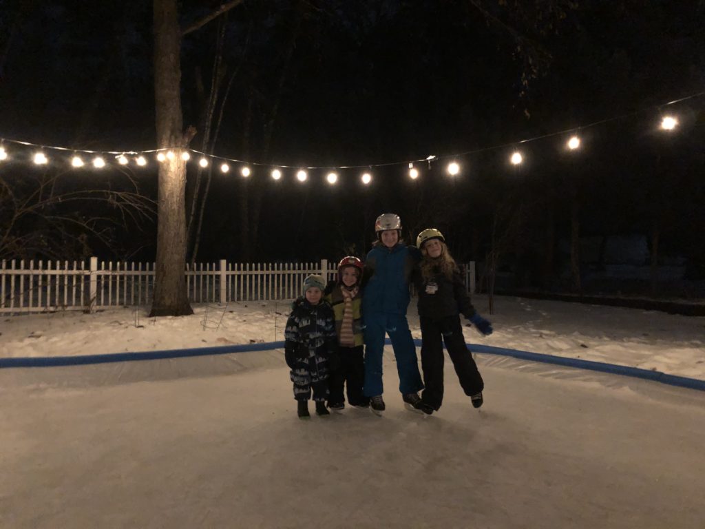 A photo of Grayson, Ainsley, Rayleigh, and Dillon skating at night with patio lights overhead.