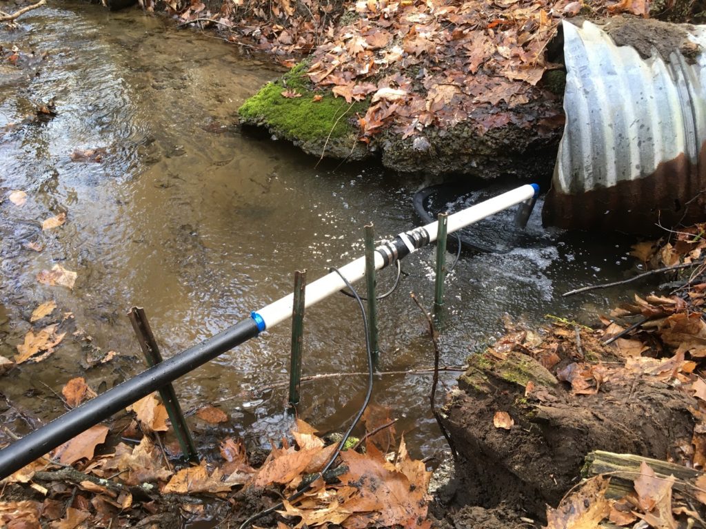 A photo of the sump pump in the stream connected to the one way valve and the pipe leading up the hill.