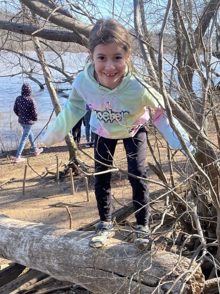 A photo of Ainsley standing on a log with the James River in the background