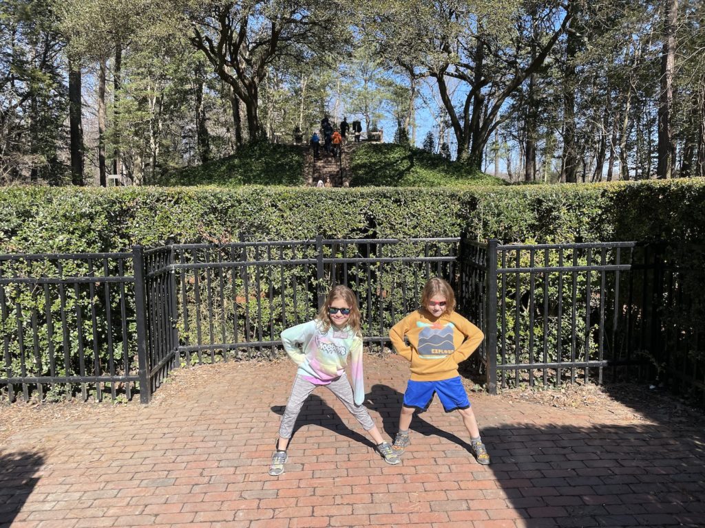 A photo of Ainsley and Grayson striking silly poses in the center of the holly maze in Colonial Williamsburg
