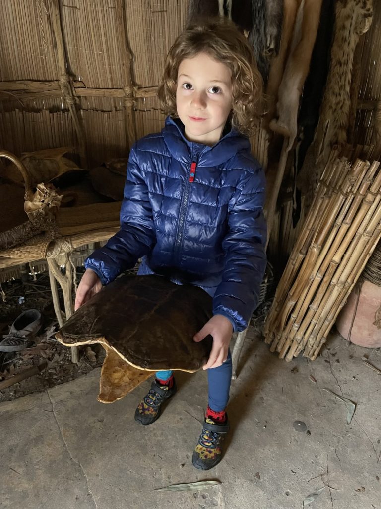A photo of Grayson holding a turtle shell inside of a yi-hakan dwelling
