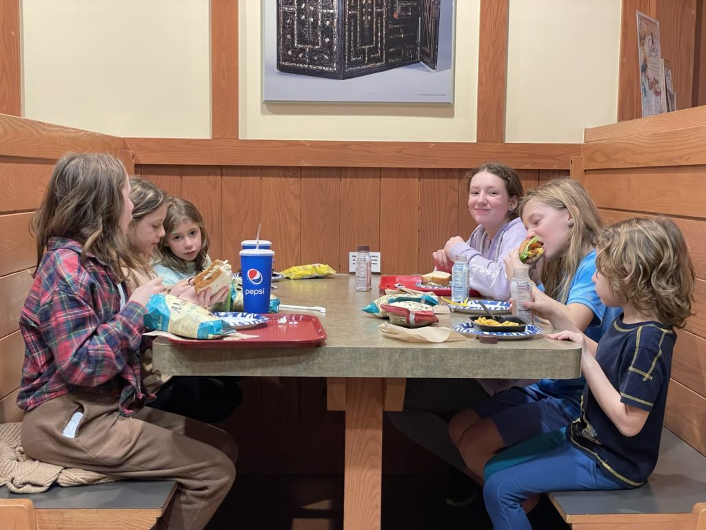 A photo of Evie, Olivia, Ainsley, Rayleigh, Dillon, and Grayson eating lunch at a booth