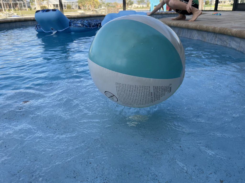 A photo of a beach ball being held in place on the surface of the water by a water jet under the surface