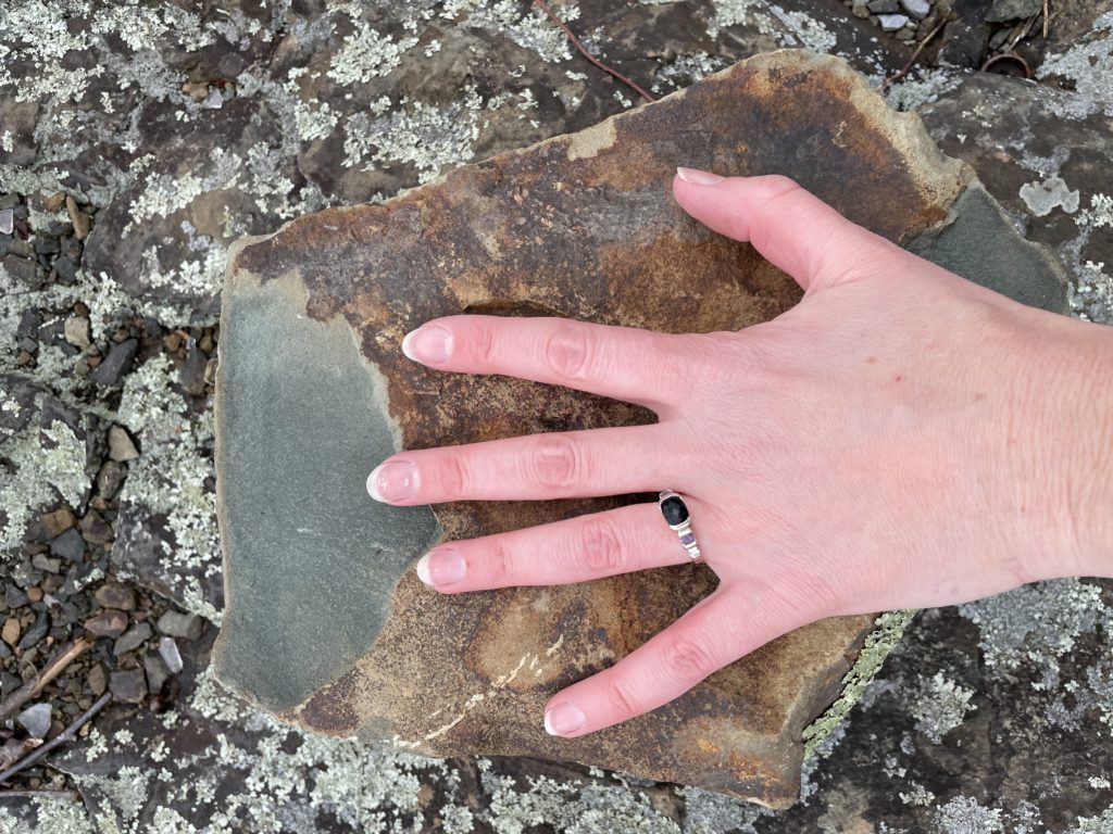 A photo of Kelsey's hand showing the relative size of a piece of basalt column that has broken off - the basalt column is slightly larger than her hand span
