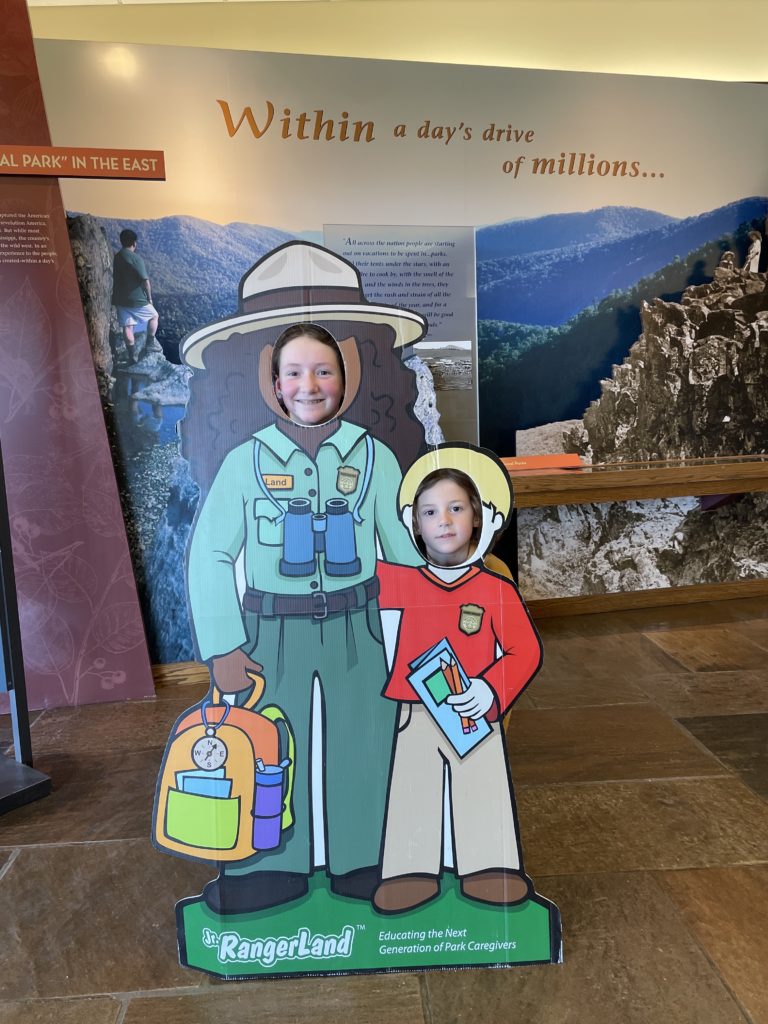 A photo of Rayleigh and Grayson posing with their faces in cutouts of a park ranger and a kid, respectively