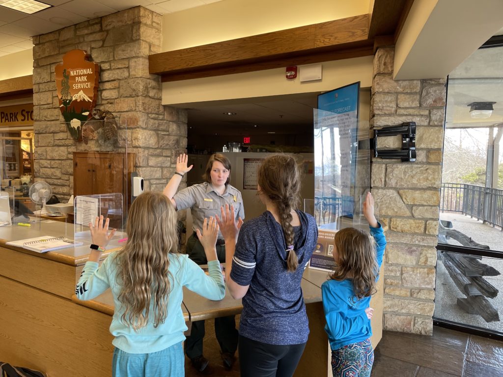 A photo of Dillon, Rayleigh, and Ainsley taking the Junior Ranger pledge with a park ranger in Shenandoah National Park