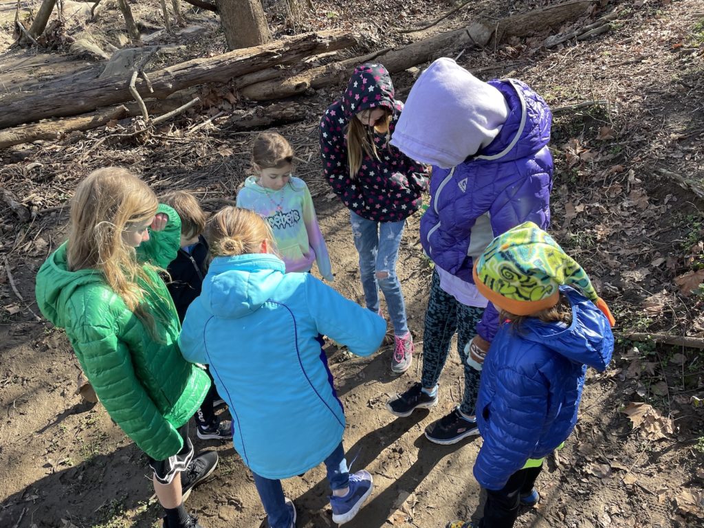 A photo of Dillon, Milo, Maisie, Ainsley, Mia, Rayleigh, and Grayson making impressions in the mud with their feet on a hiking path