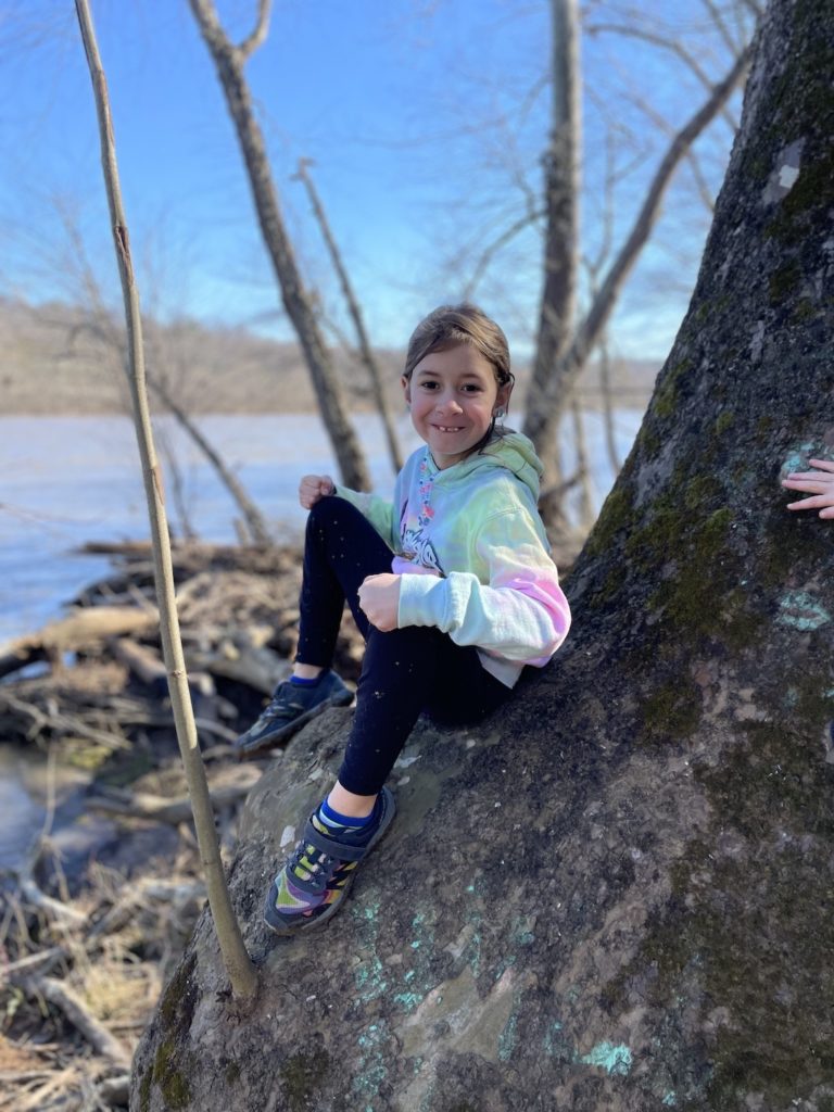 A photo of Ainsley sitting on a tree on the bank of the James River