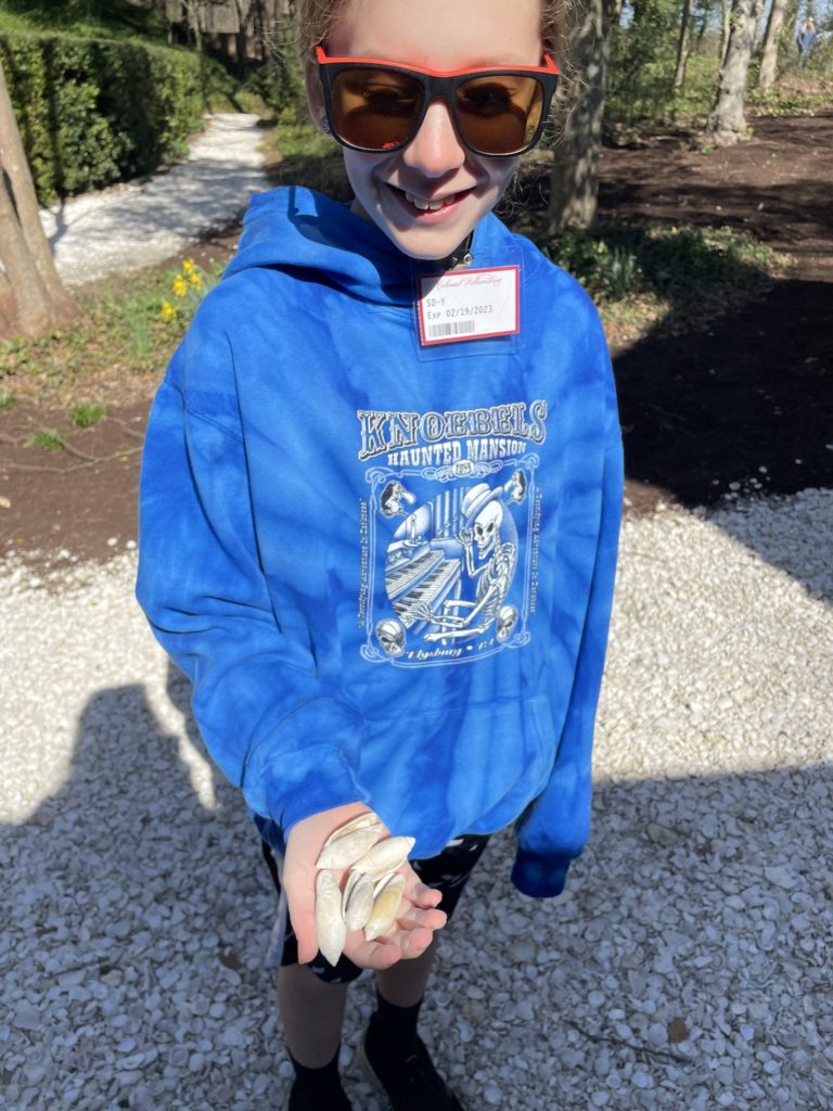 A photo of Dillon showing off five similar seashells picked from a walking path in Colonial Williamsburg