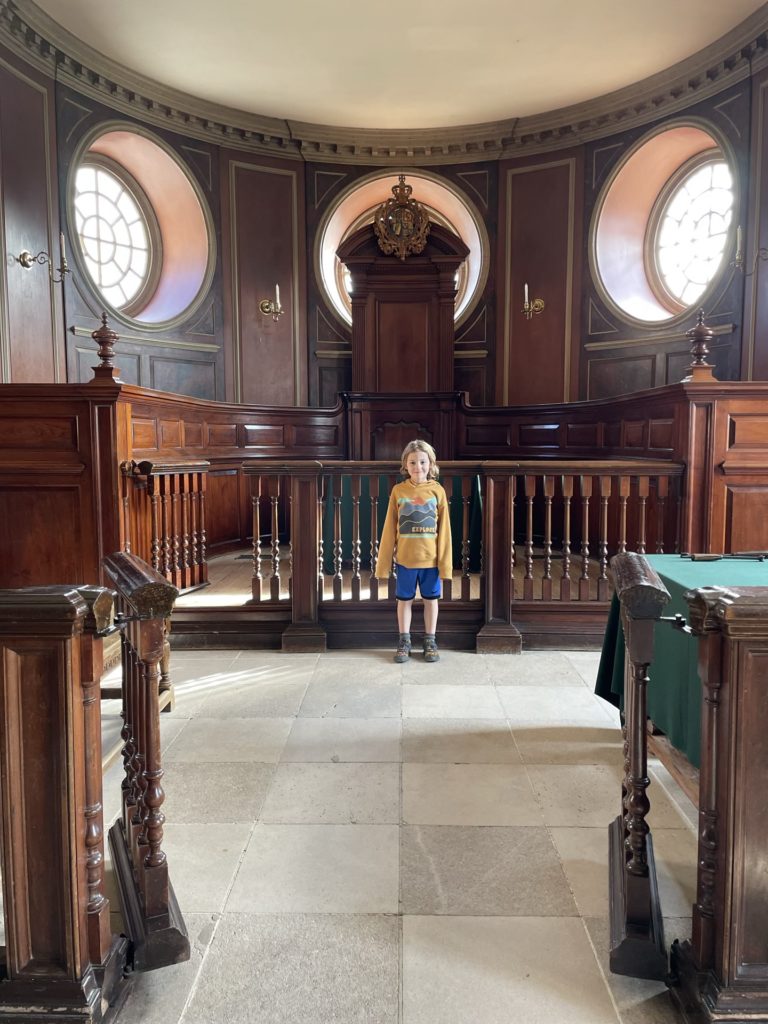 A photo of Grayson standing in front of the judge's chair in the capitol at Colonial Williamsburg