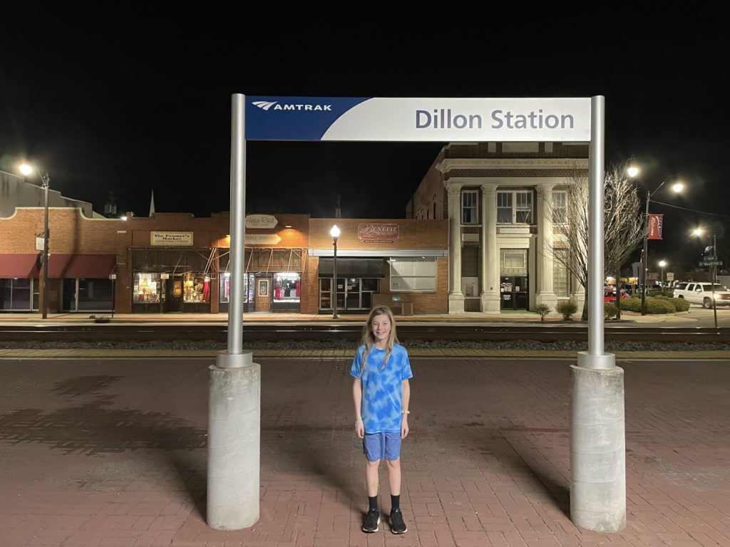 A photo of Dillon standing under the sign for the Dillon Amtrak Station