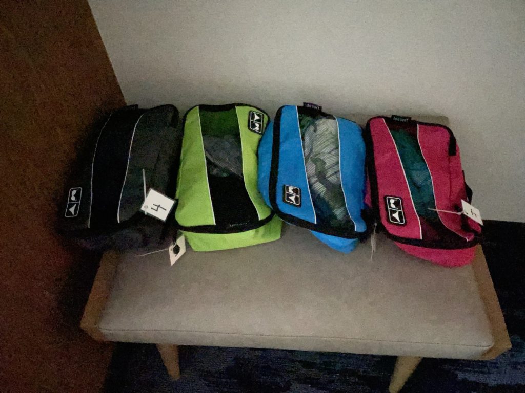 A photo of black, green, blue, and red clothes bags lined up on a hotel bench