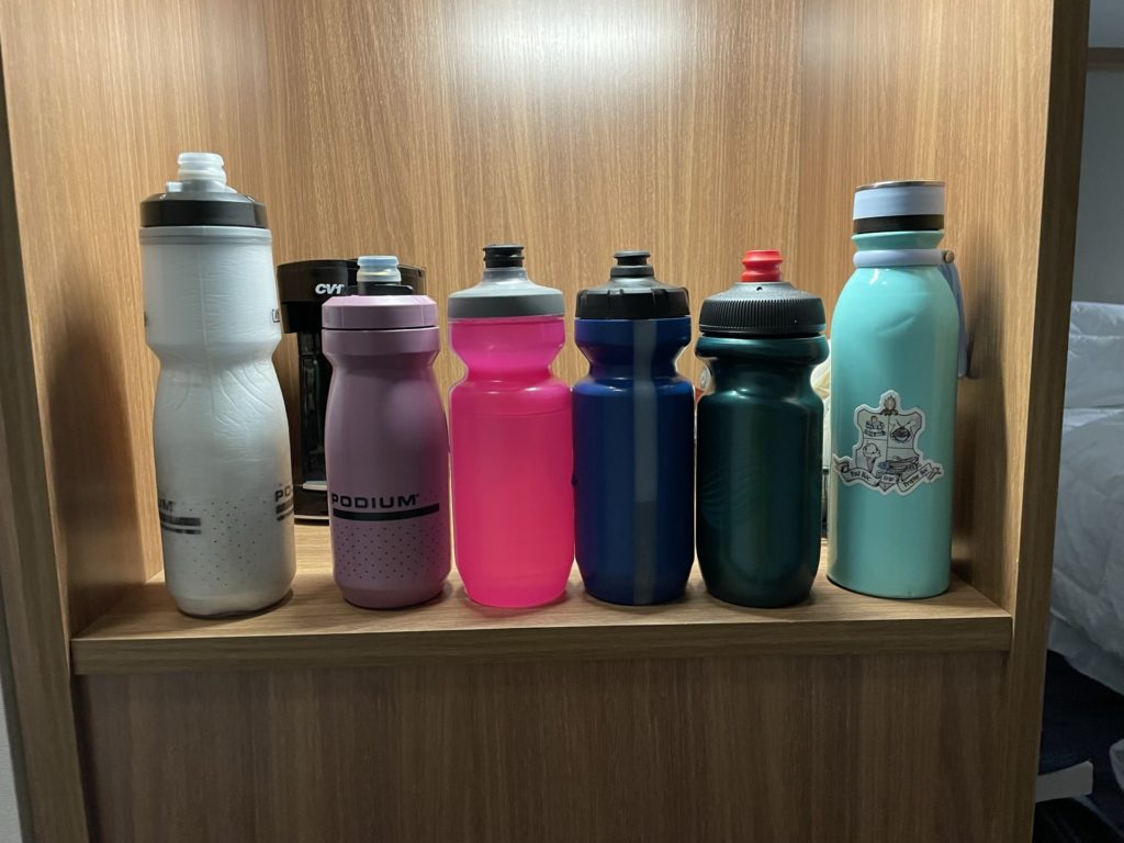 A photo of a white, purple, pink, blue, green, and teal water bottle sitting on a hotel shelf