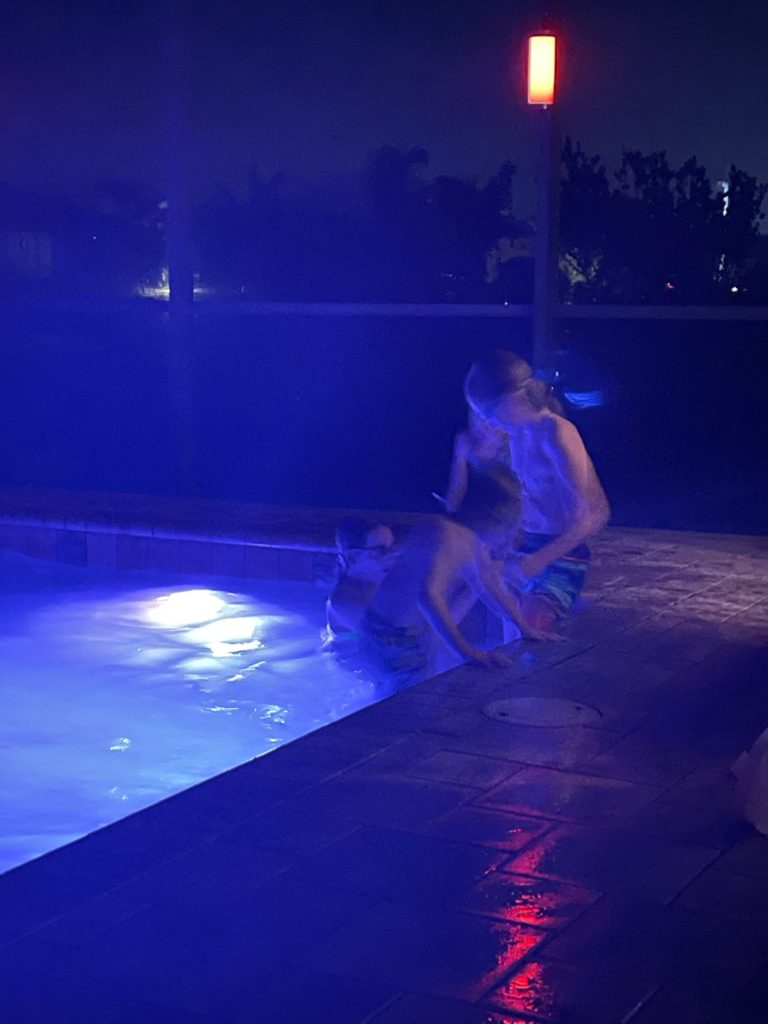 A photo of Rayleigh, Grayson, Ainsley, and Dillon swimming in a pool at night