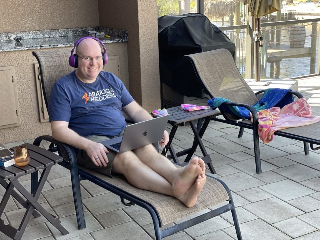 A photo of Kevin sitting on a chair on the pool deck with a laptop on his lap and headphones on his head.