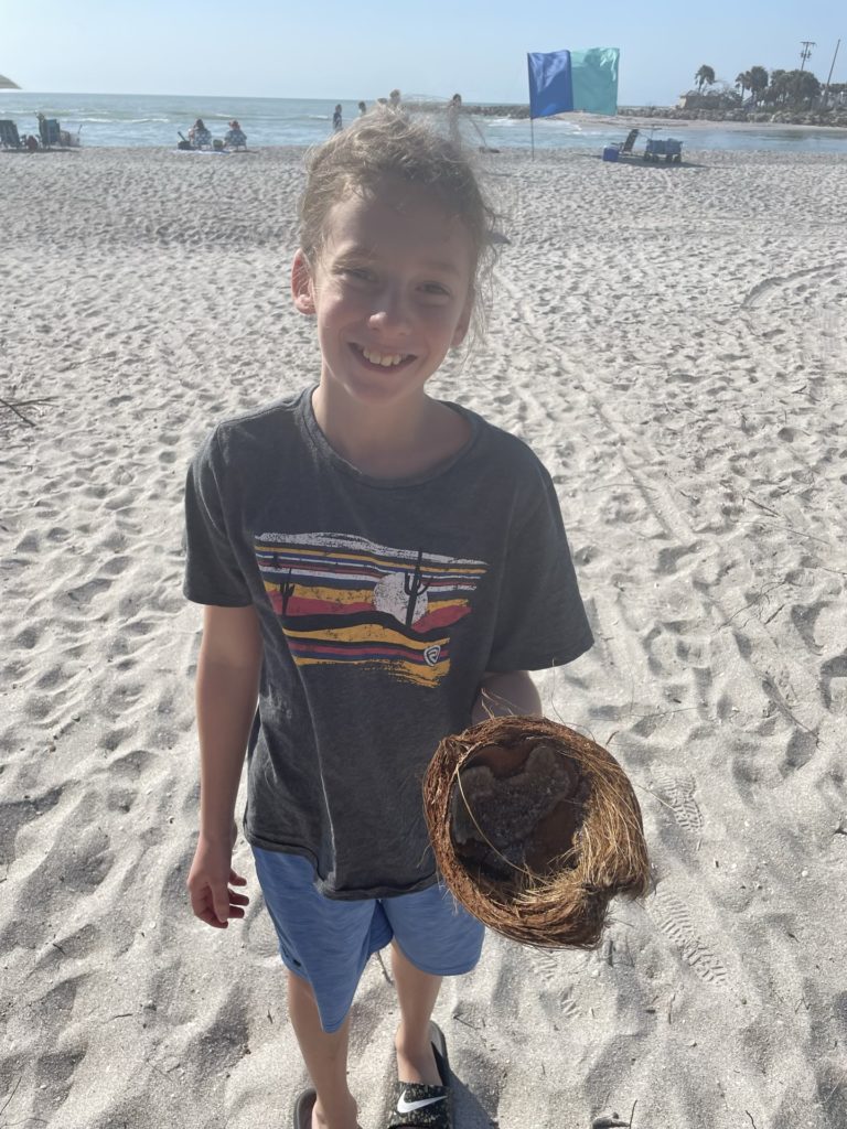 A photo of Dillon holding the husk of a coconut on the beach