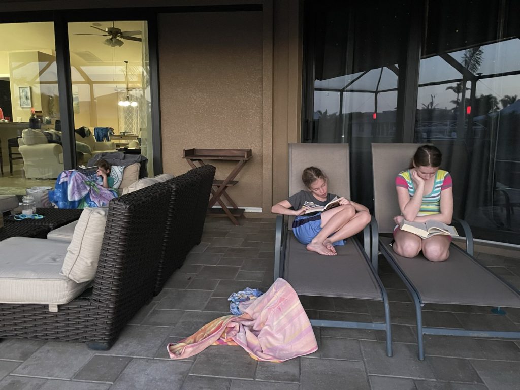 A photo of Ainsley, Dillon, and Rayleigh reading books on the pool deck