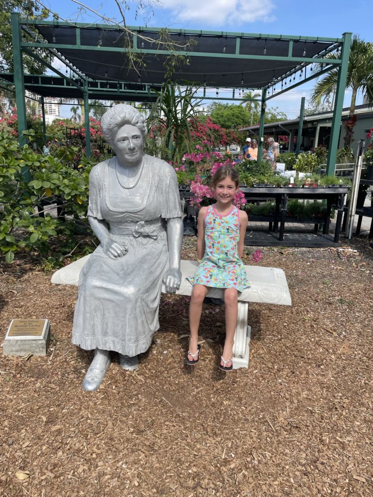 A photo of Ainsley sitting on a bench next to a statue of Mina Edison