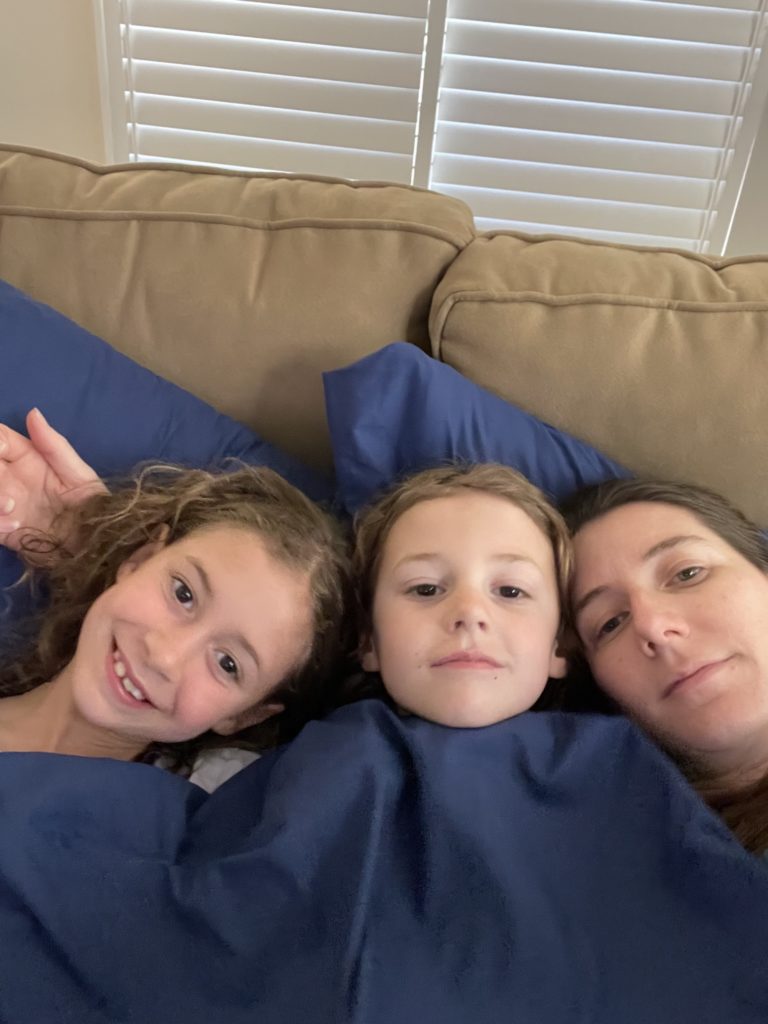 A photo of Ainsley, Grayson, and Kelsey snuggling under a blanket