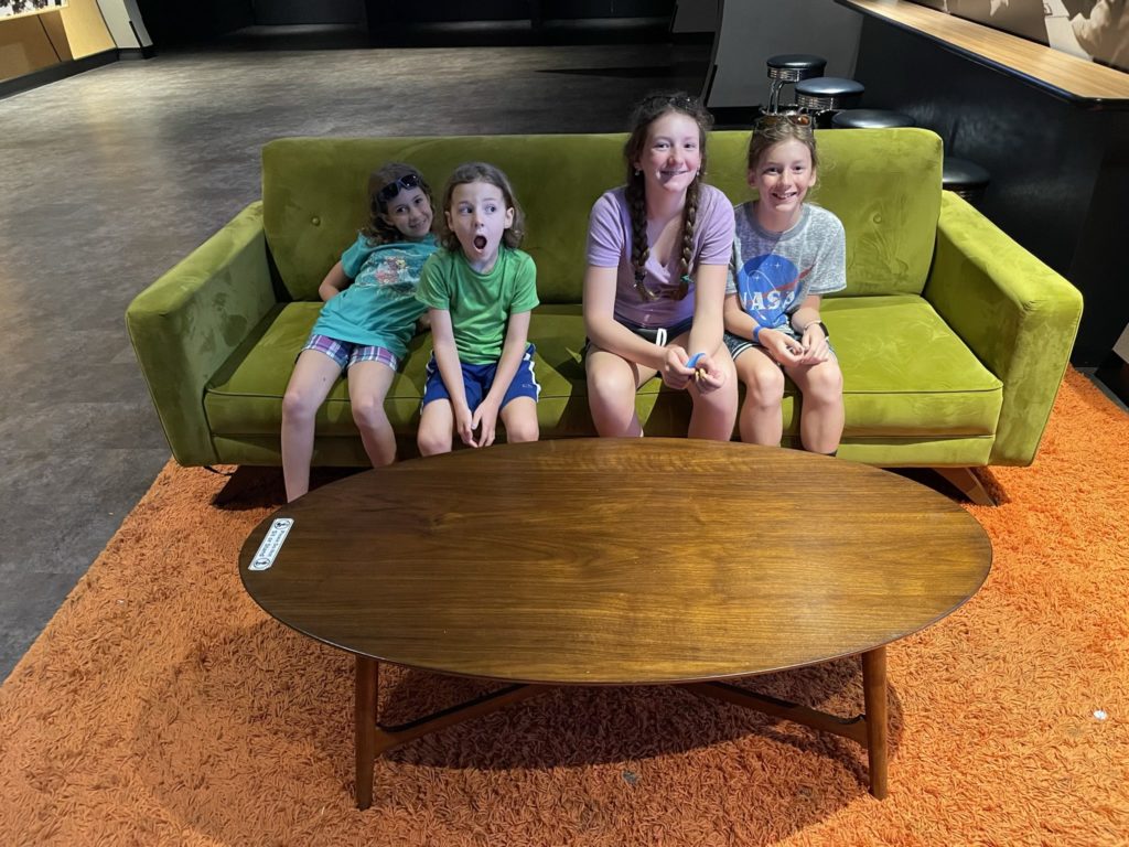 A photo of Ainsley, Grayson, Rayleigh, and Dillon on a 1960s-style lime green couch on orange shag carpeting