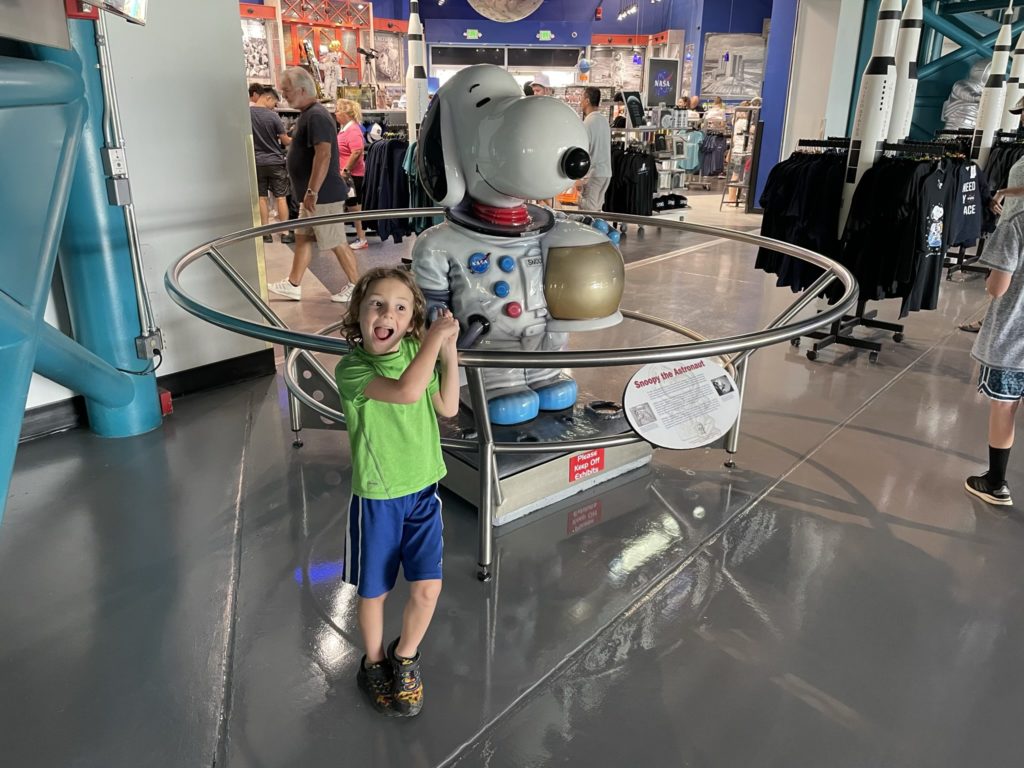 A photo of Grayson excitedly pointing to a statue of Snoopy dressed like an astronaut