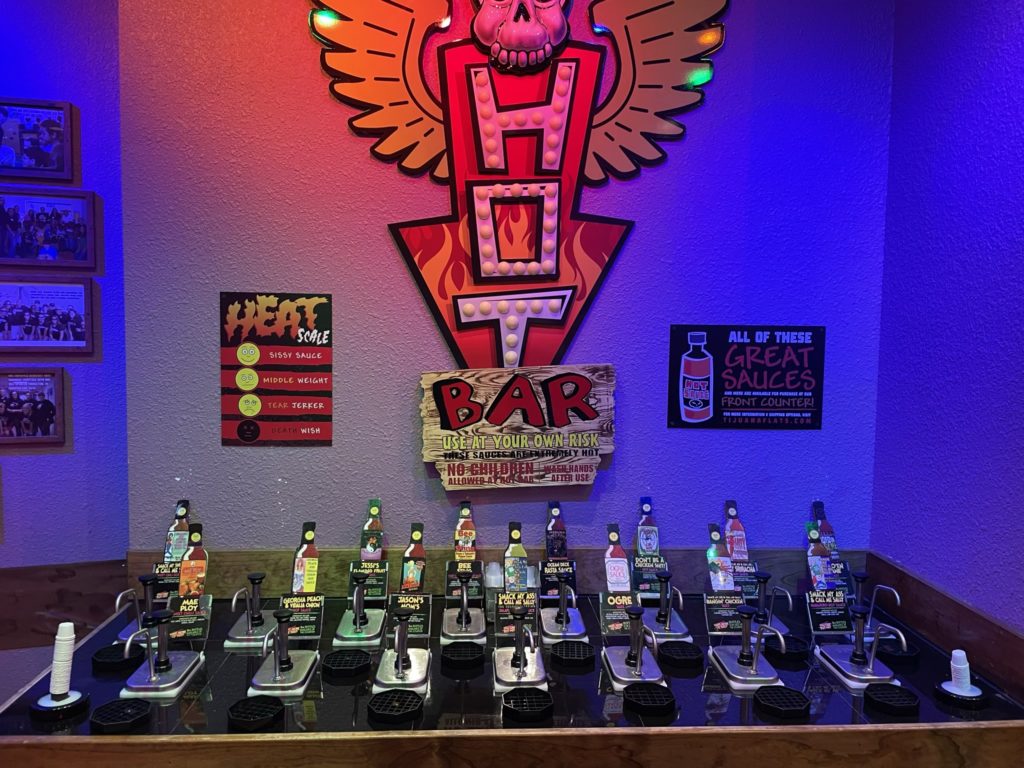 A photo of a hot sauce bar at a taco shop, which says "Hot bar: use at your own risk!"