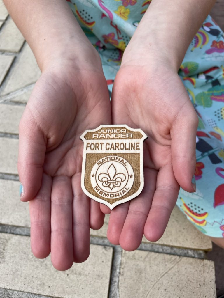 A photo of Ainsley holding a Fort Caroline Junior Ranger badge