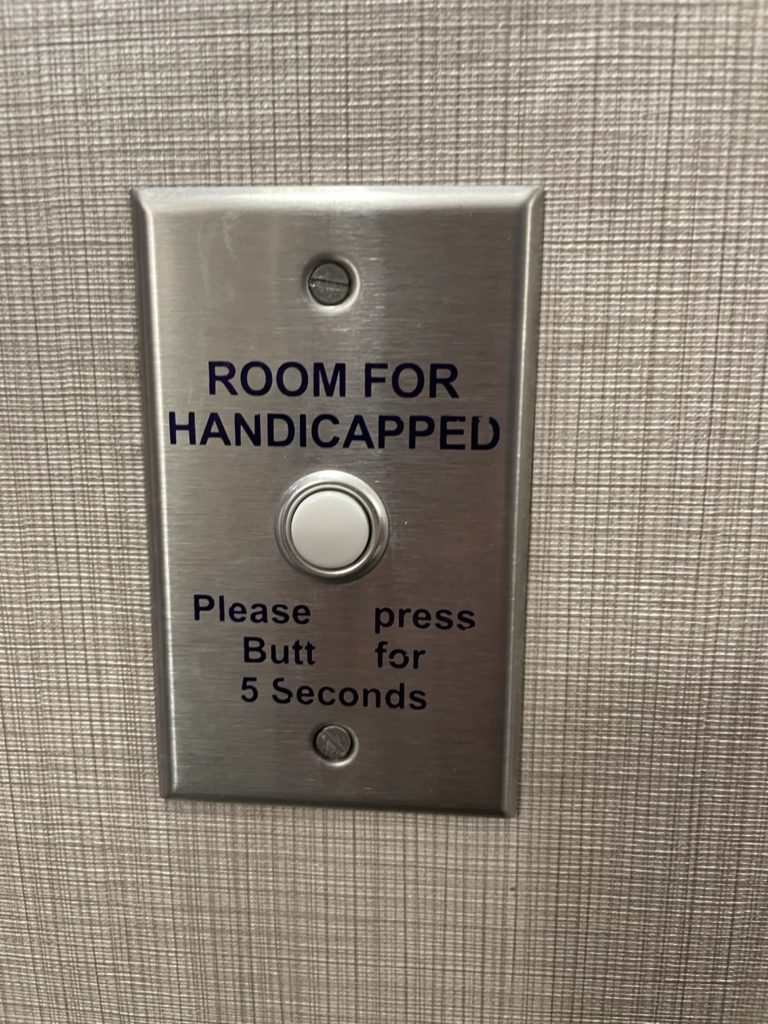 A photo of a hotel room doorbell that says "Room for handicapped: please press butt for 5 seconds"