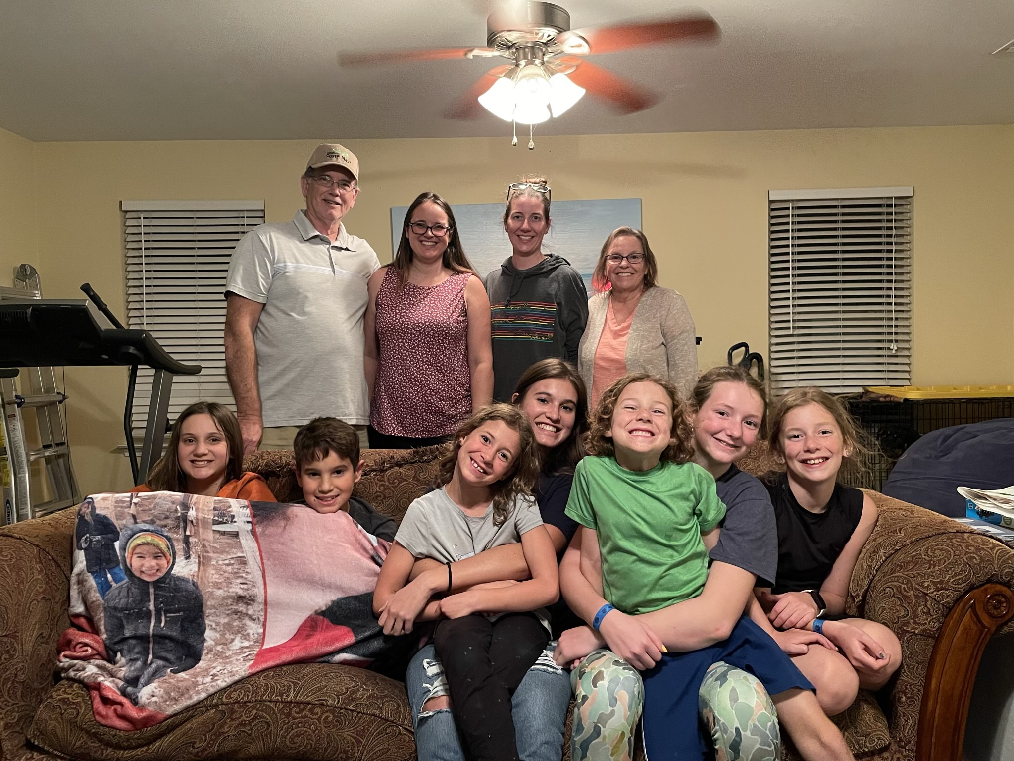A photo of Uncle Ken, Kim, Kelsey, Aunt Karen, Niala, Riker, Ainsley, Kahlan, Grayson, Rayleigh, and Dillon with the kids on a couch and the adults standing at Kim's house