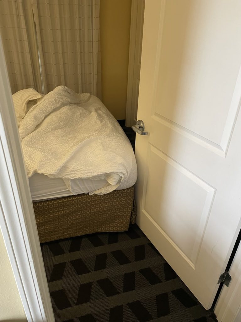 A photo of a door to a hotel room being unable to close because the bed is in the way