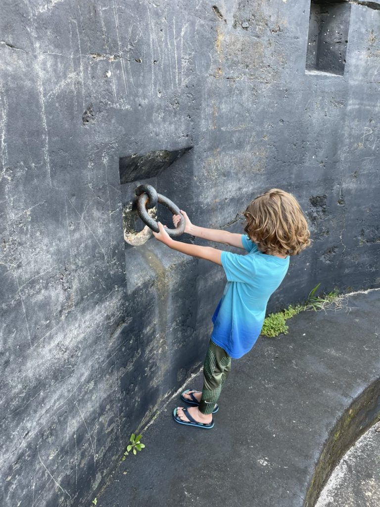 A photo of Grayson pulling on a large metal ring attached to a concrete wall