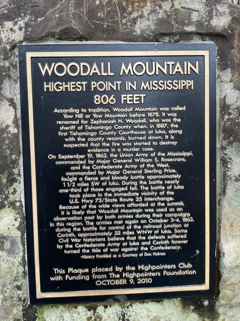 A photo of a plaque embedded in a boulder that says "Woodall Mountain: highest point in Mississippi, 806 feet"