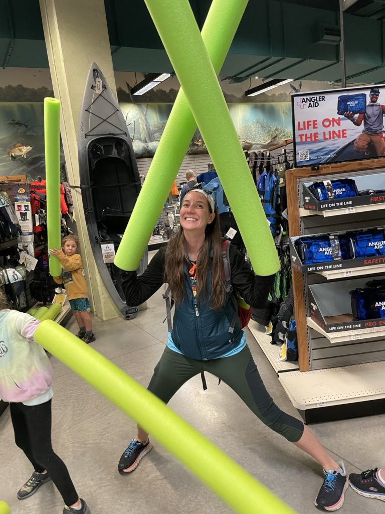 A photo of Kelsey with giant pool noodles on her hands getting ready to battle inside the Bass Pro Shops store, with Grayson and Ainsley preparing to do the same
