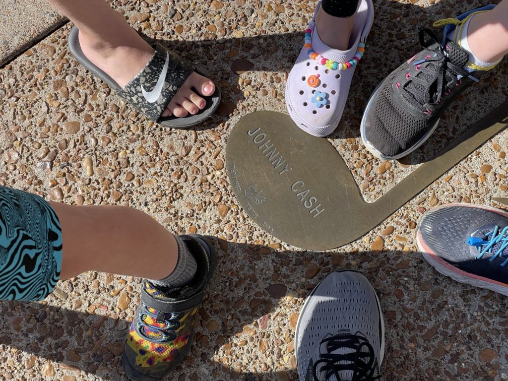 A photo of Grayson, Ainsley, Dillon, Rayleigh, Kelsey, and Kevin's feet next to Johnny Cash's brass note embedded in Beale Street