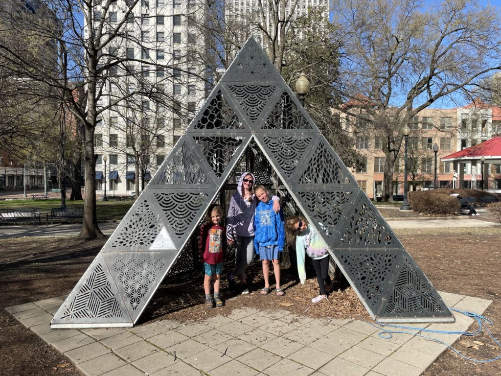 A photo of Grayson, Rayleigh, Dillon, and Ainsley in a pyramid-shaped sculpture in a park