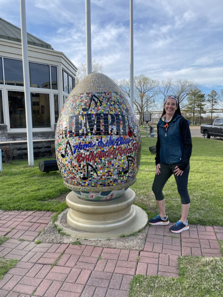 A photo of Kelsey standing next to a giant egg with a mosaic pattern that features music notes and says "Memphis: Home of the blues, birthplace of rock and roll"