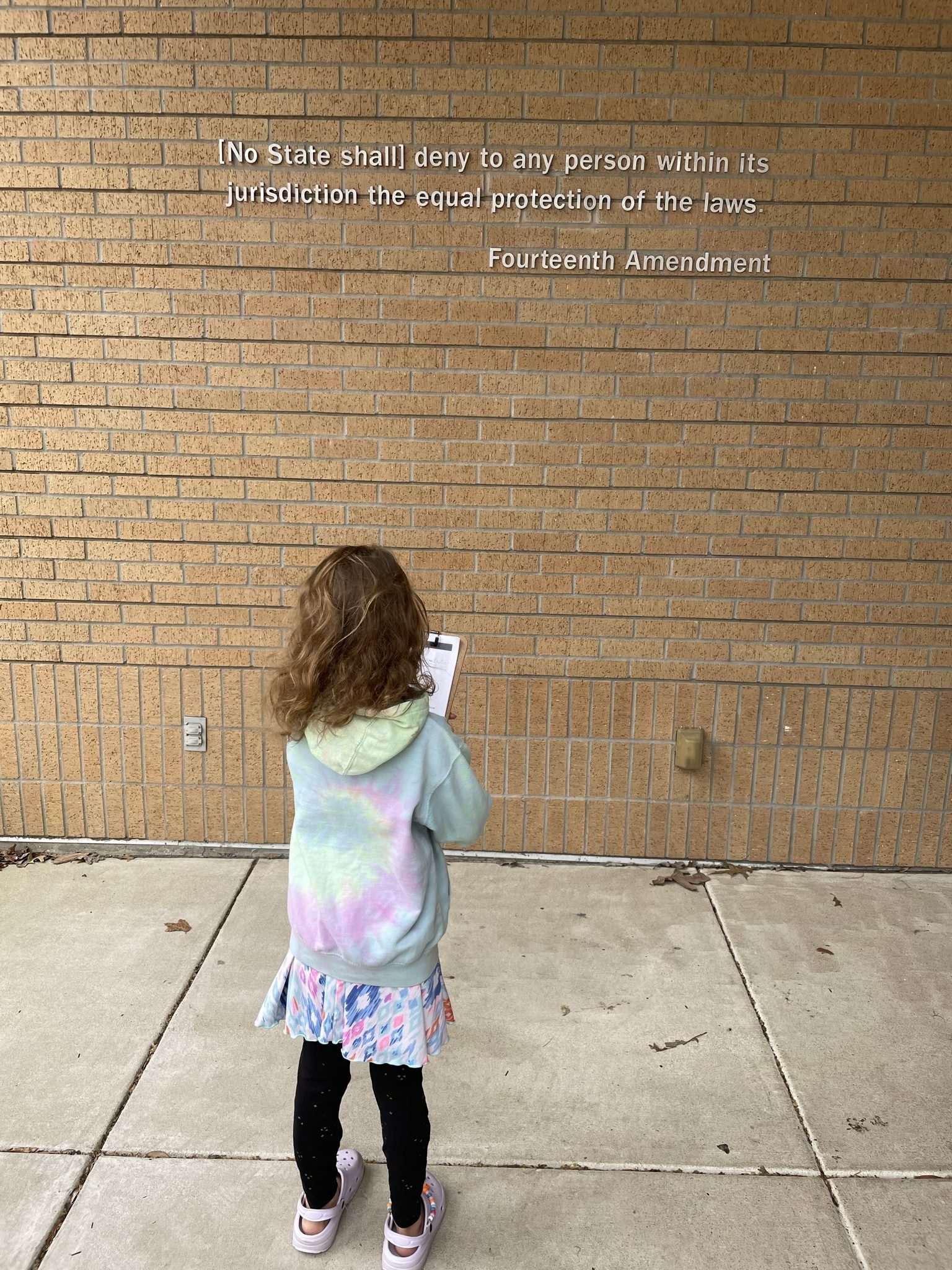 A photo of Ainsley standing in front of a quote on the wall of a brick building that says \