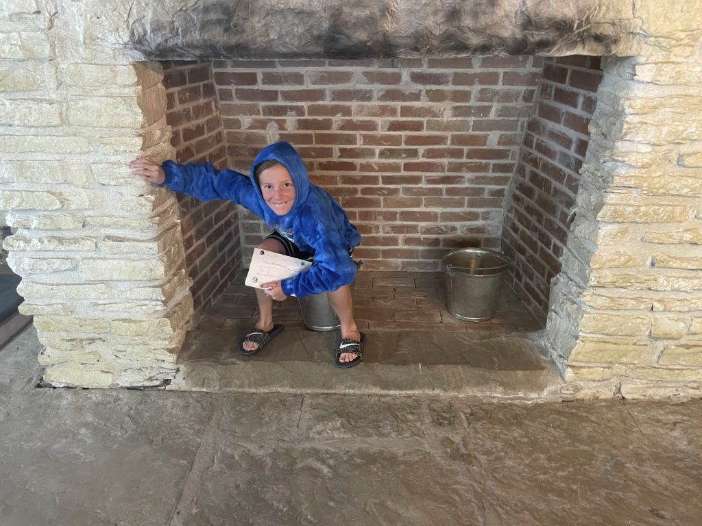 A photo of Dillon pretending to poop in a bucket in a fireplace in the Fort Smith jail.