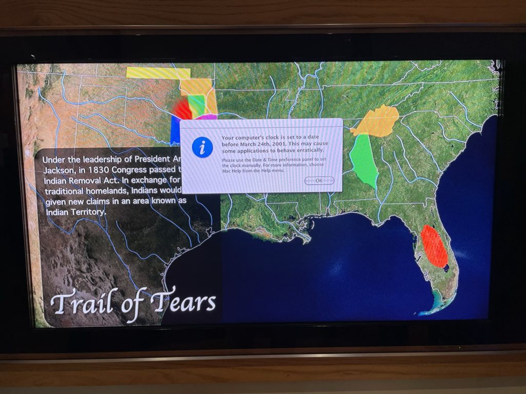 A photo of a screen with an educational display about the trail of tears with an error message dialog that says "Your computer's clock is set to a date before March 24, 2001. This may cause some applications to behave erratically."