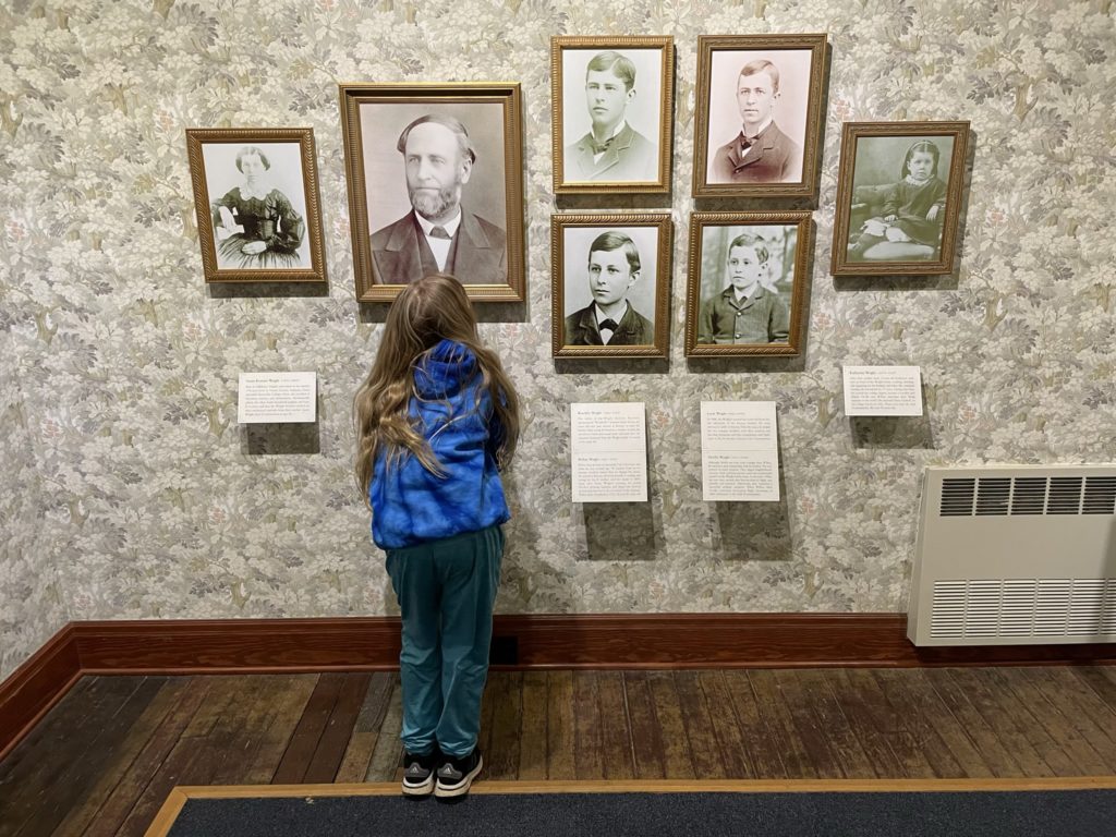 A photo of Dillon filling out information in his Junior Ranger book in front of a wall of photographs of the Wright family
