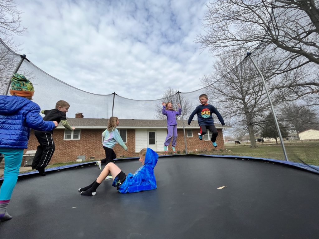 A photo of Grayson, Peter, Ainsley, Dillon, Nora, and Oliver jumping on a trampoline