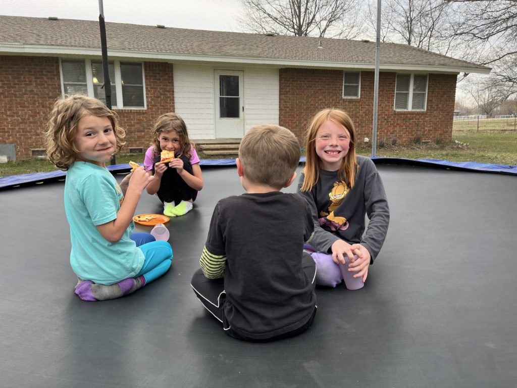 A photo of Grayson, Ainsley, Peter, and Nora eating pizza on a trampoline