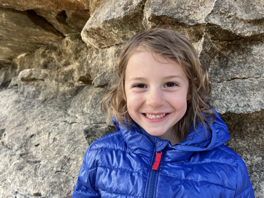 A phto of Grayson smiling wearing a coat in front of a rock outcropping
